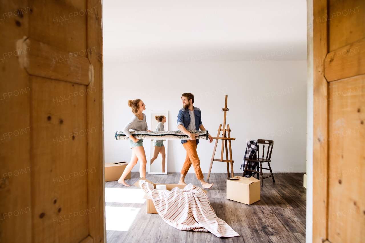 Young married couple moving in new house, carrying a carpet together.