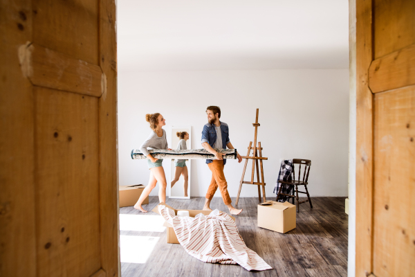 Young married couple moving in new house, carrying a carpet together.