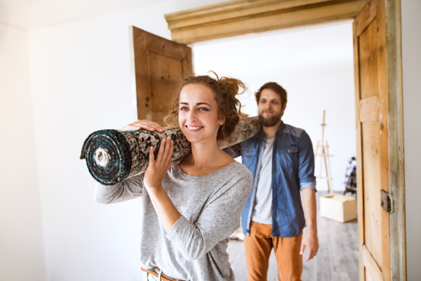 Young married couple moving in new house, carrying a carpet together.