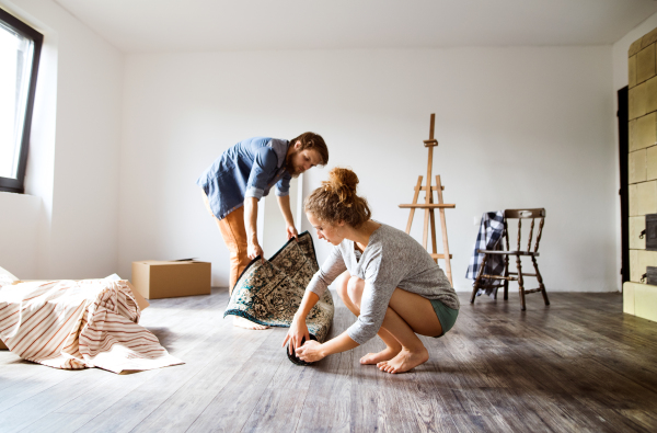 Young married couple moving in new house, rolling out carpet.