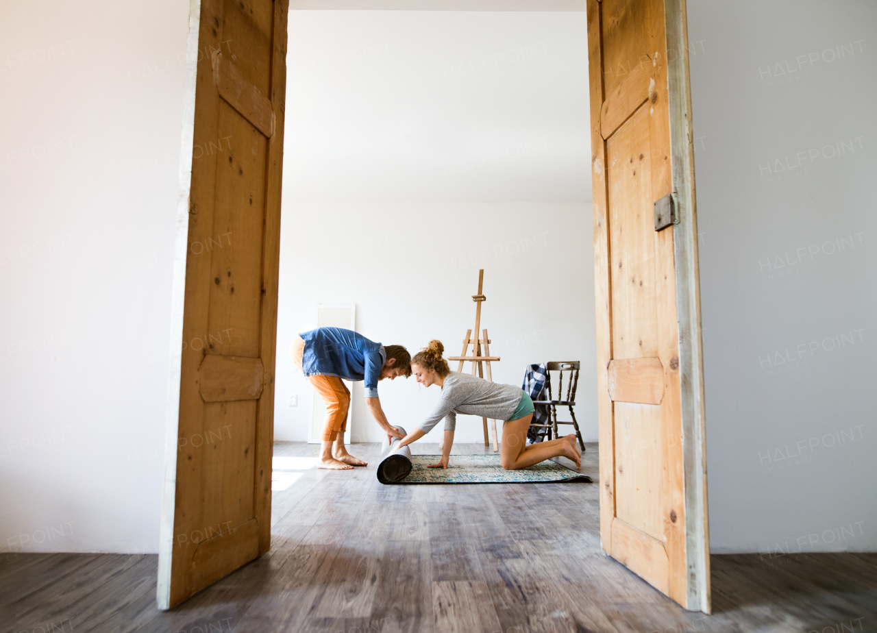 Young married couple moving in new house, rolling out carpet.