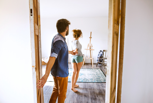 Young married couple moving in new house, woman leading man by the hand, entering through the door.