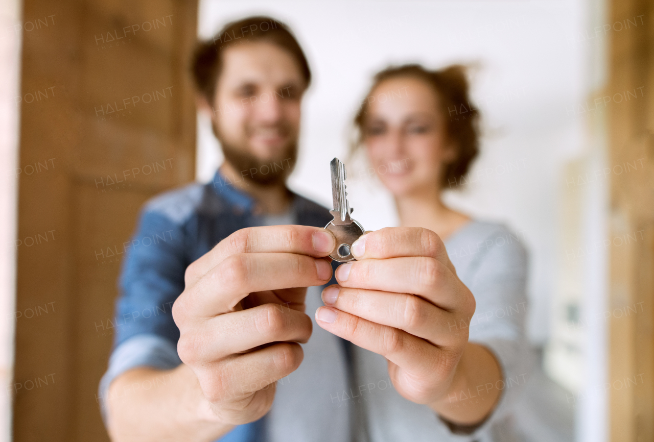 Young married couple moving in a new house, entering through the door, holding a key together.