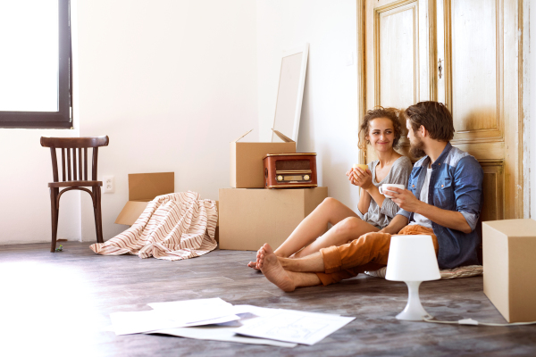 Young married couple moving in a new house, sitting on the floor at the old wooden door, drinking coffee, resting