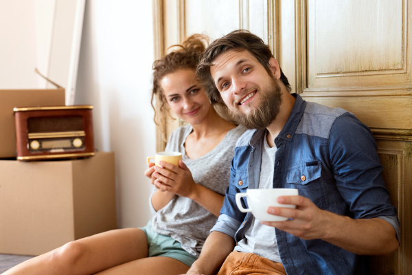 Young married couple moving in new house, sitting on the floor against old wooden door, drinking coffee, resting