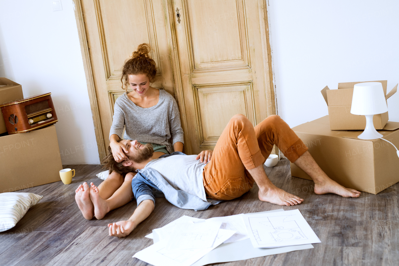 Young married couple moving in new house, lying on the floor near cardboard boxes, resting.