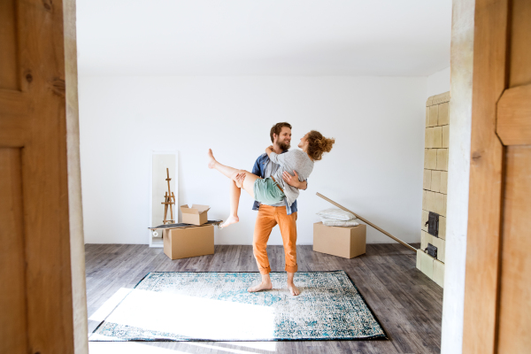 Young married couple moving in a new house, man carrying woman in his arms.