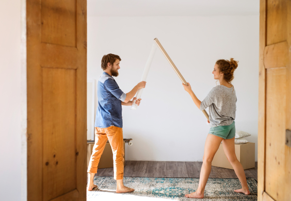 Young married couple moving in new house, fighting with rolls of wrapping paper.