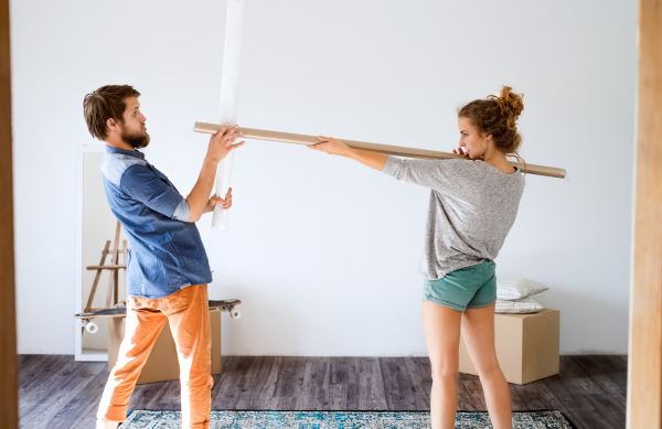 Young married couple moving in new house, fighting with rolls of wrapping paper.