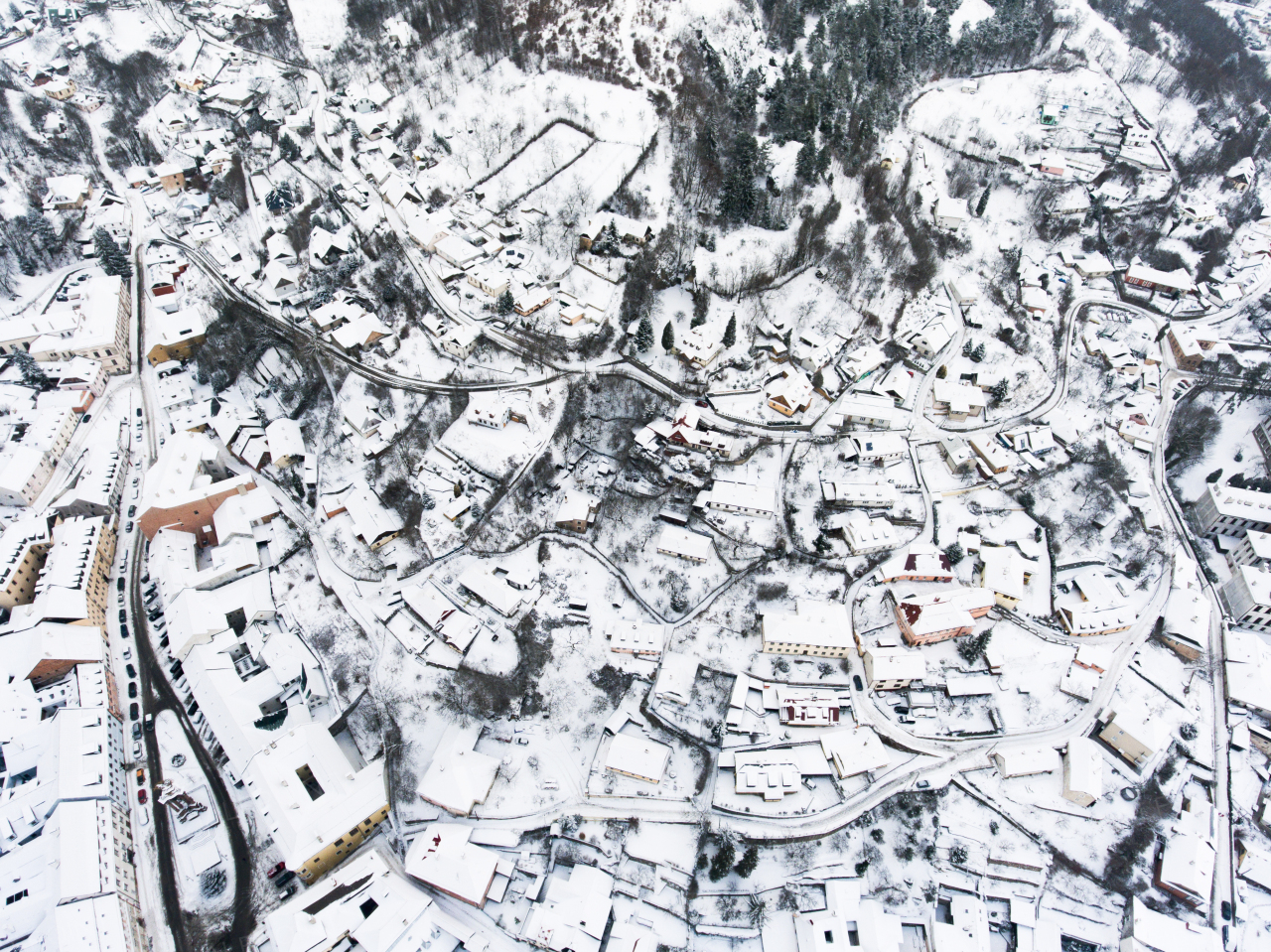 Aerial view of small town with many hills and forest surrounding it. Winter time.