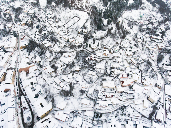 Aerial view of small town with many hills and forest surrounding it. Winter time.