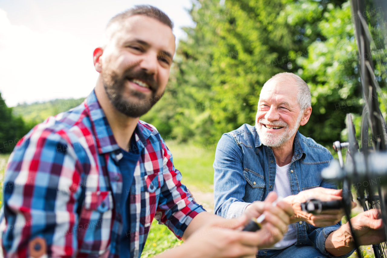 An adult hipster son and senior father repairing bicycle outside on a sunny summer day.