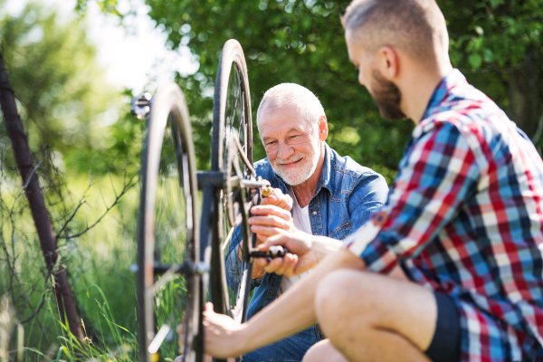 An adult hipster son and senior father repairing bicycle outside on a sunny summer day.