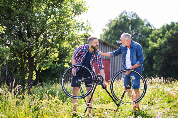 An adult hipster son and senior father repairing bicycle puncture outside on a sunny summer day.