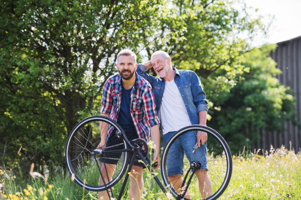 An adult hipster son and senior father repairing bicycle puncture outside on a sunny summer day.