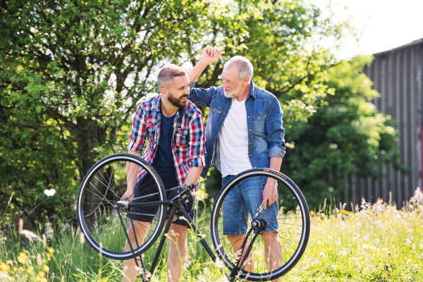 An adult hipster son and senior father repairing bicycle outside on a sunny summer day.