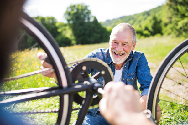 A senior father and his unrecognizable son repairing bicycle outside on a sunny day.