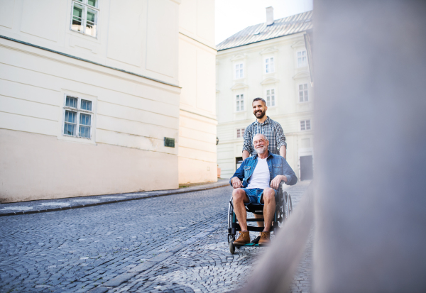 An adult hipster son with his senior father in wheelchair on a walk in town. Copy space.