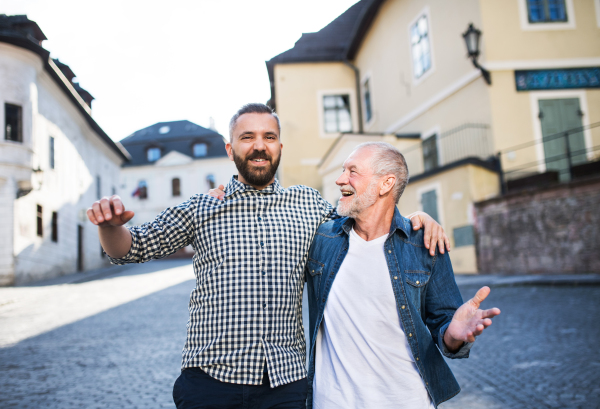 A happy adult hipster son with his senior father in town, walking arm in arm.