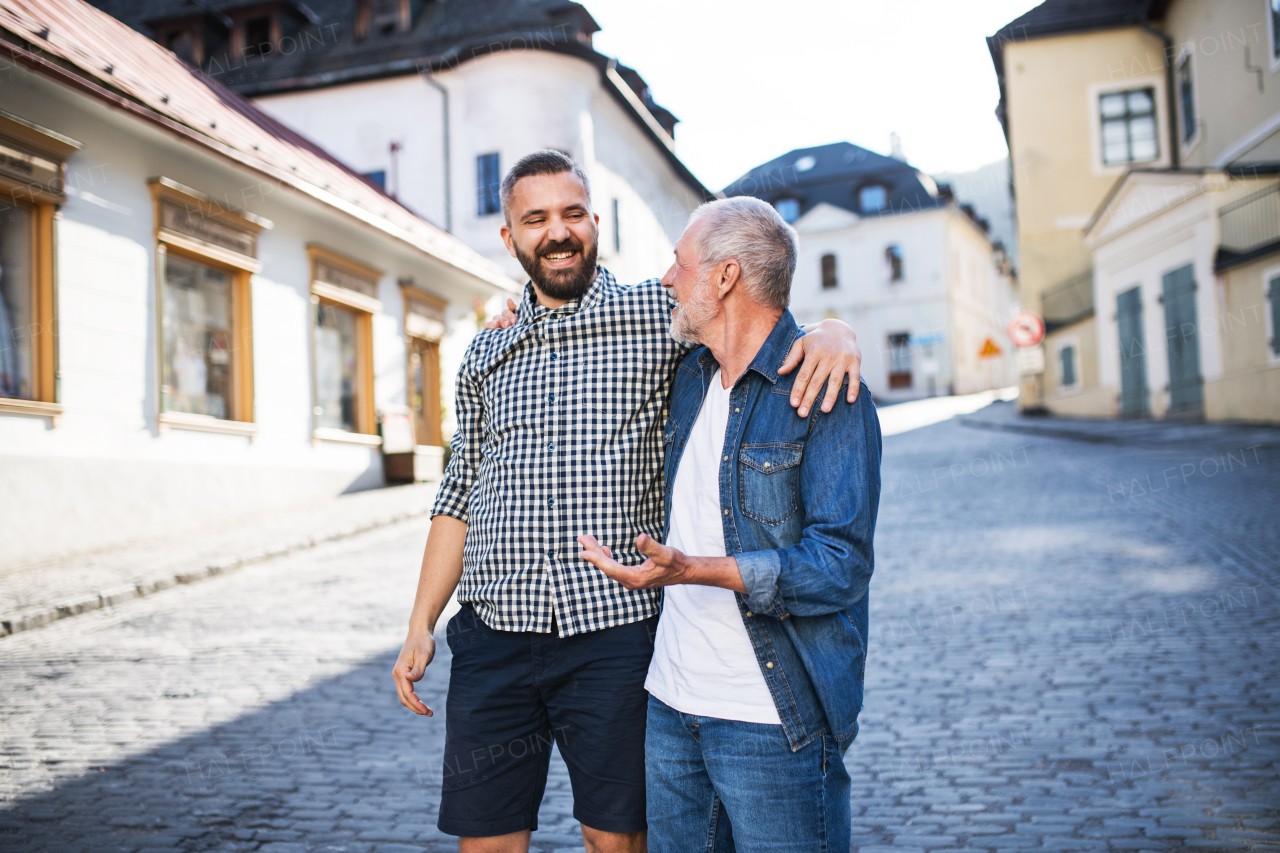 A happy adult hipster son with his senior father in town, walking arm in arm.