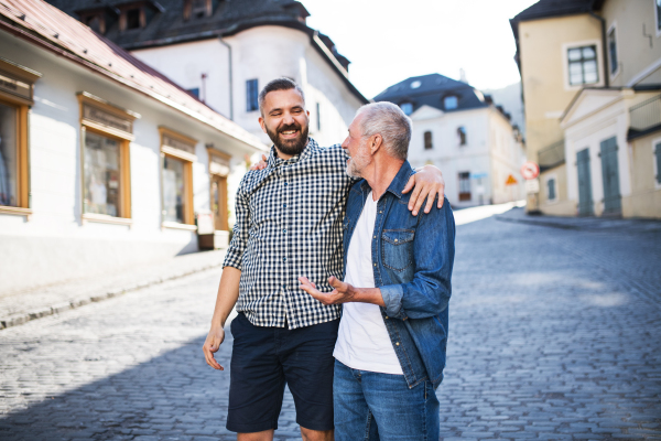 A happy adult hipster son with his senior father in town, walking arm in arm.