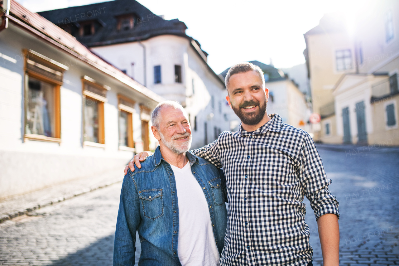 A happy adult hipster son with his senior father in town, walking arm in arm.