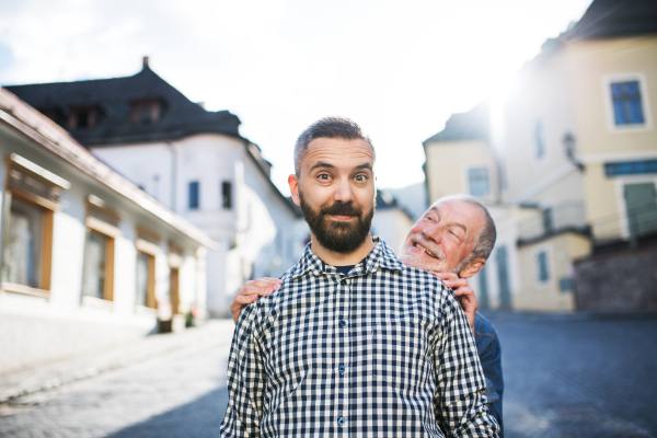 A happy adult hipster son with his senior father on a walk in town, having fun.