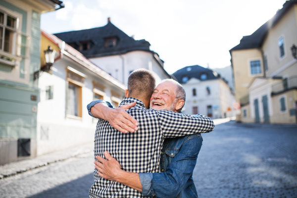 An adult hipster son and his happy senior father in town, hugging.