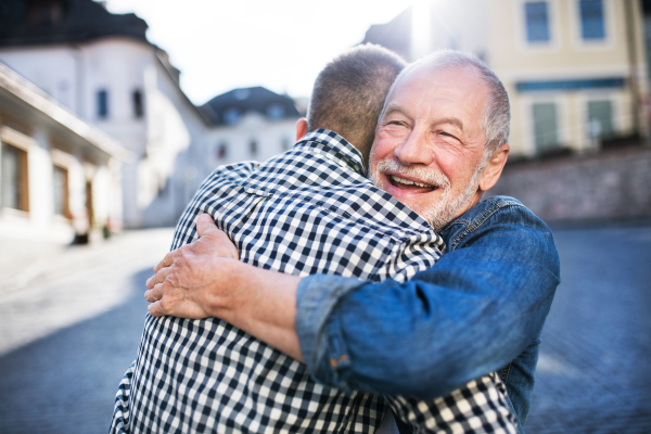 An adult hipster son and his happy senior father in town, hugging.