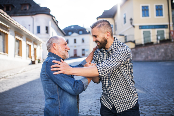 An adult hipster son and his overjoyed senior father in town, greeting each other.