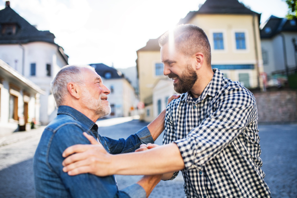 An adult hipster son with his senior father on a walk in town, greeting.