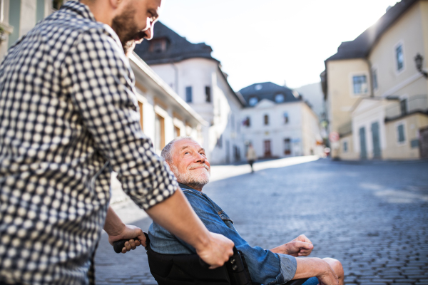 An unrecognizable adult hipster son with his senior father in wheelchair on a walk in town.