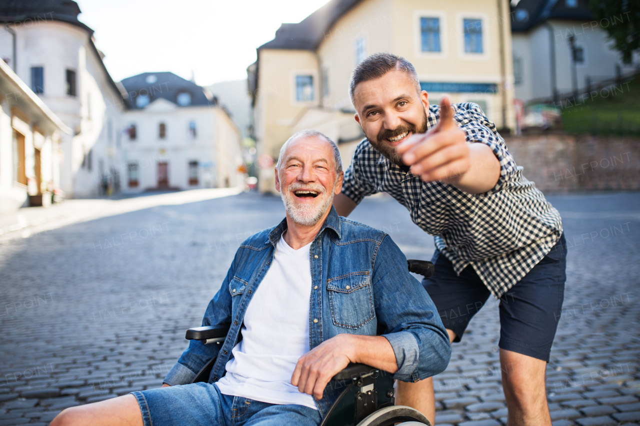 An adult hipster son with his senior father in wheelchair on a walk in town, pointing to something.