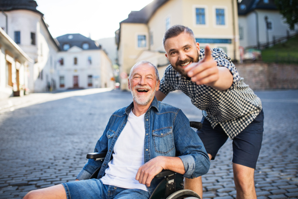 An adult hipster son with his senior father in wheelchair on a walk in town, pointing to something.