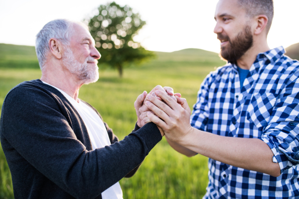 An adult hipster son with his senior father on a walk in nature at sunset. Close up.