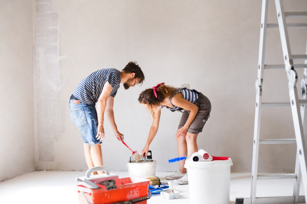 Beautiful young couple having fun and painting walls using paint roller in their new house. Home makeover and renovation concept.