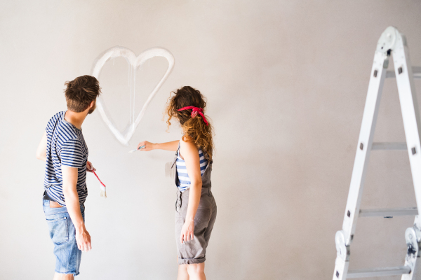 Beautiful young couple having fun and painting heart on the wall of their new house. Home makeover and renovation concept.