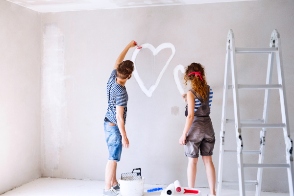 Beautiful young couple having fun and painting heart on the wall of their new house. Home makeover and renovation concept.