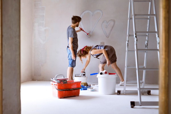 Beautiful young couple having fun and painting hearts on the wall of their new house. Home makeover and renovation concept.