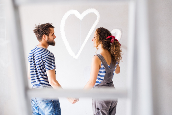 Beautiful young couple having fun and painting heart on the wall of their new house. Home makeover and renovation concept.