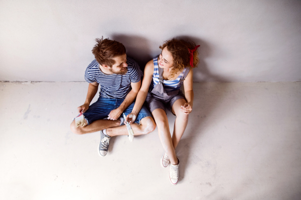 Beautiful young couple in love having fun, painting walls of their new house with paintbrushes. Home makeover and renovation concept.