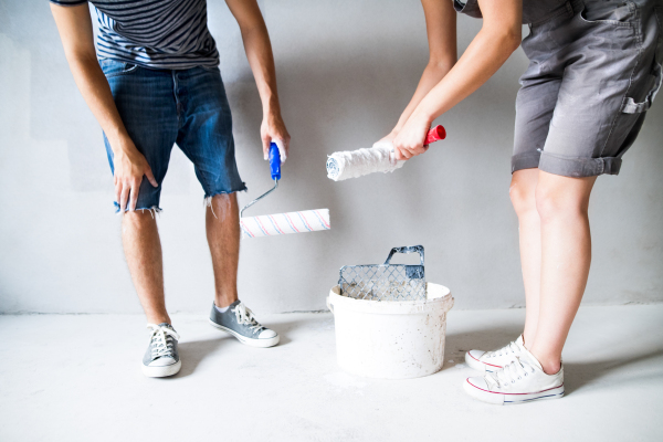 Unrecognizable young couple having fun and painting walls using paint roller in their new house. Home makeover and renovation concept.