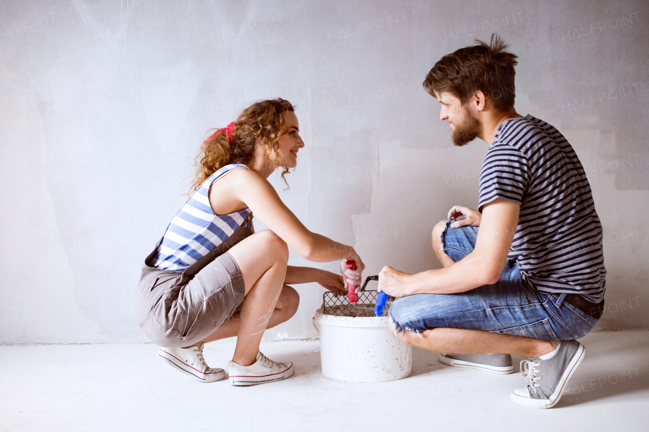 Beautiful young couple in love having fun, painting walls of their new house with paint rollers. Home makeover and renovation concept.