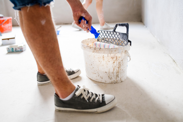 Unrecognizable young couple having fun and painting walls using paint roller in their new house. Home makeover and renovation concept.