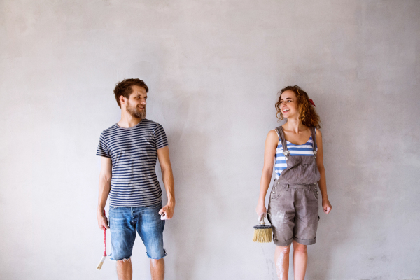 Beautiful young couple in love having fun, painting walls of their new house with paintbrushes. Home makeover and renovation concept.