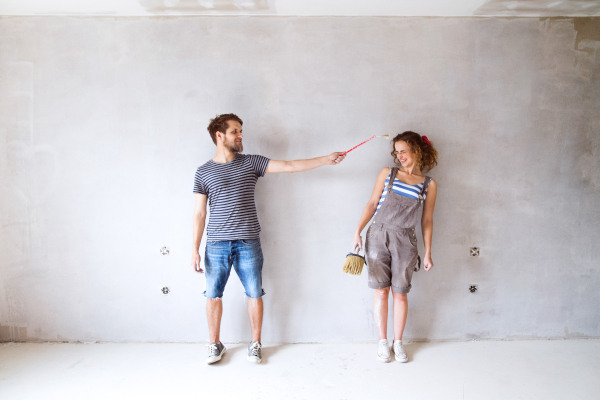 Beautiful young couple in love having fun, painting walls of their new house with paintbrushes. Home makeover and renovation concept.