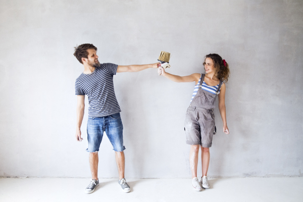 Beautiful young couple in love having fun, painting walls of their new house with paintbrushes, making funny face. Home makeover and renovation concept.