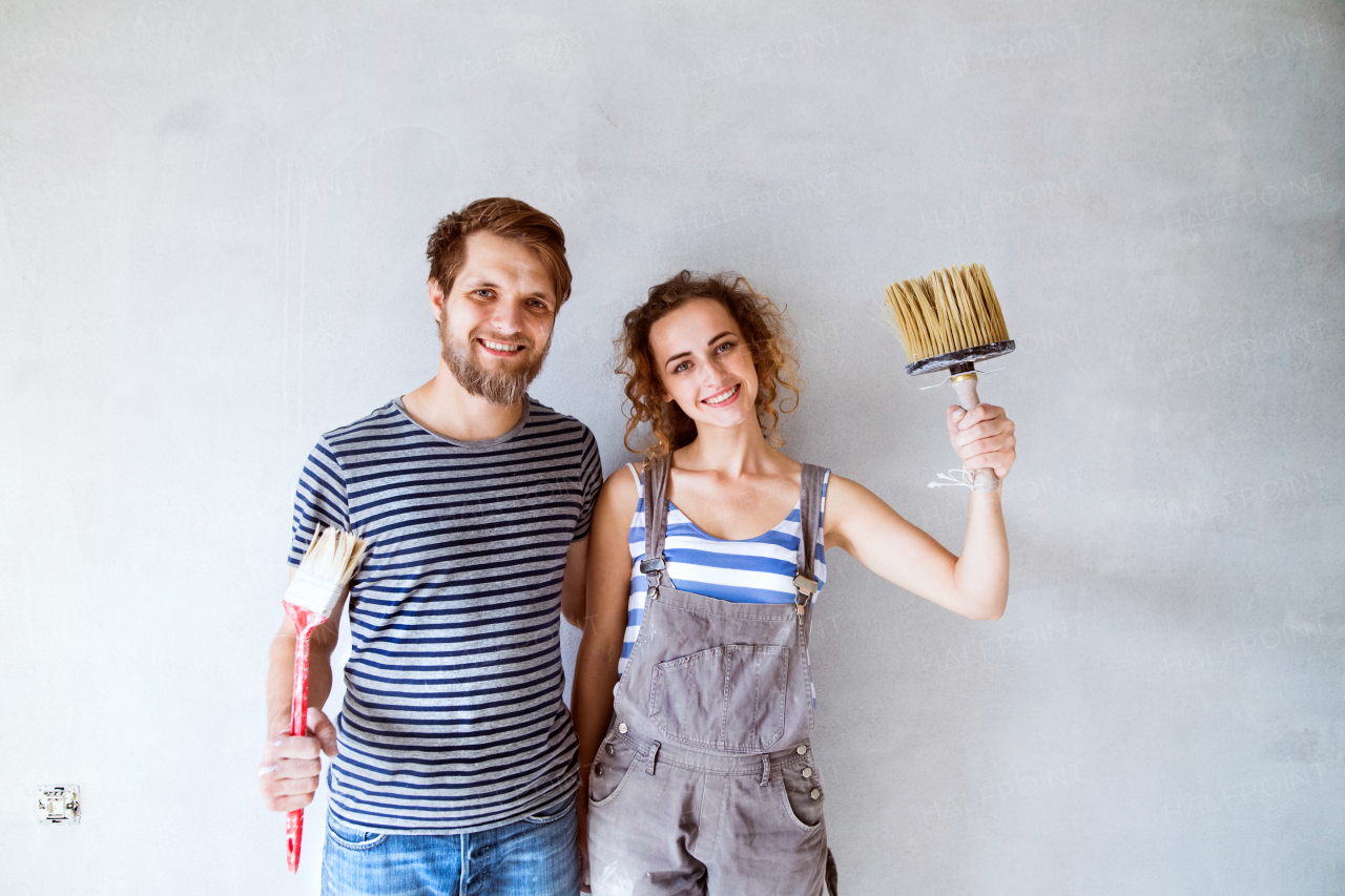 Beautiful young couple in love having fun, painting walls of their new house with paintbrushes. Home makeover and renovation concept.