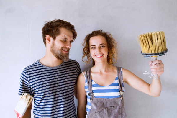 Beautiful young couple in love having fun, painting walls of their new house with paintbrushes. Home makeover and renovation concept.