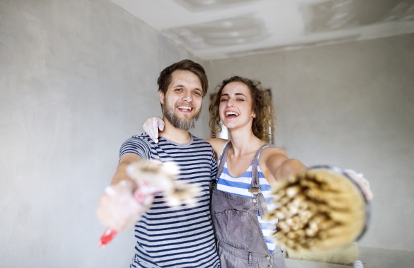 Beautiful young couple in love having fun, painting walls of their new house with paintbrushes. Home makeover and renovation concept.